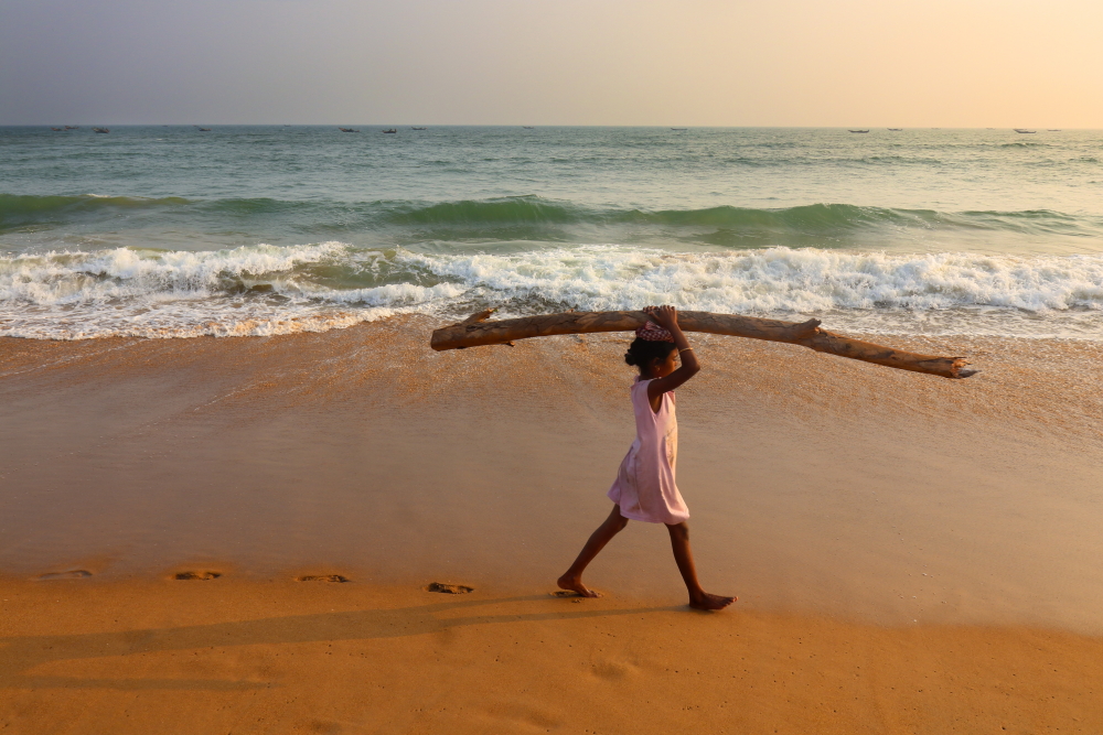 A girl carrying a log in Penthakata sea beach