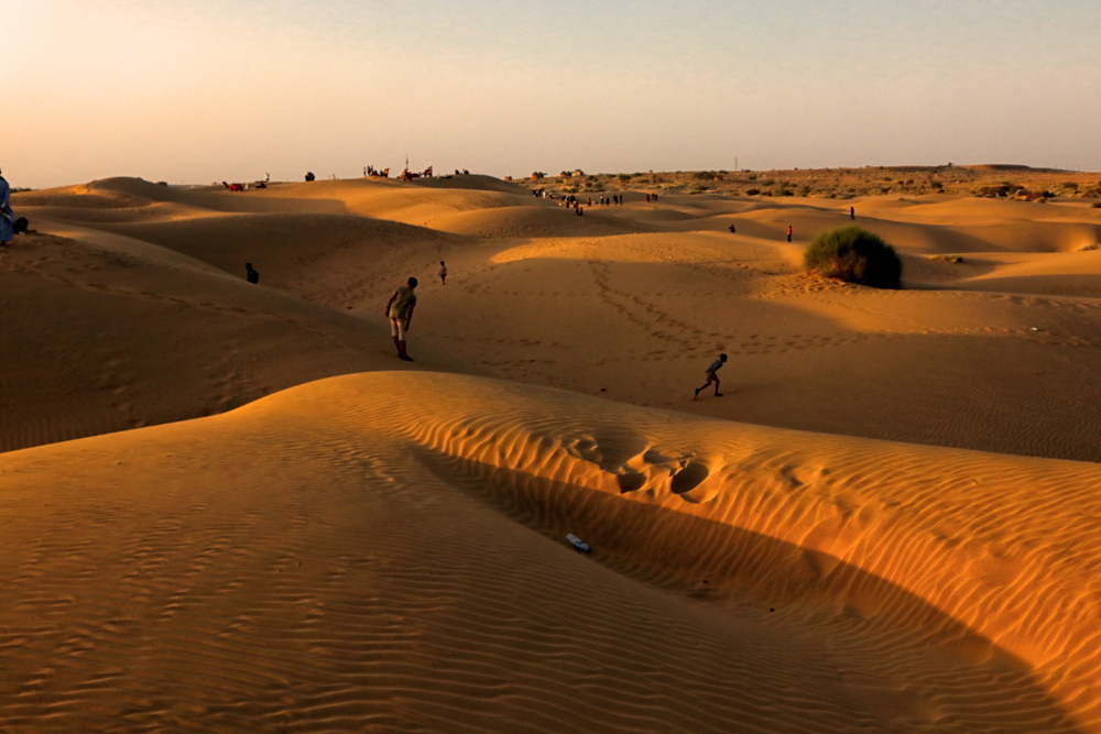 An image showing a stretch of undulating golden sand dunes in Sam in Rajasthan. Few local kids were enjoying running over the dunes.