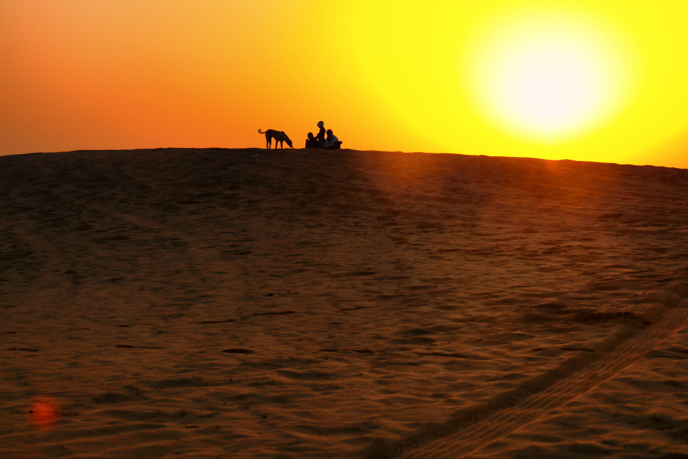 Early morning sun in Thar desert. THe silhouette of tourists sitting on the top of a dune while sun is raging high in the backdrop.