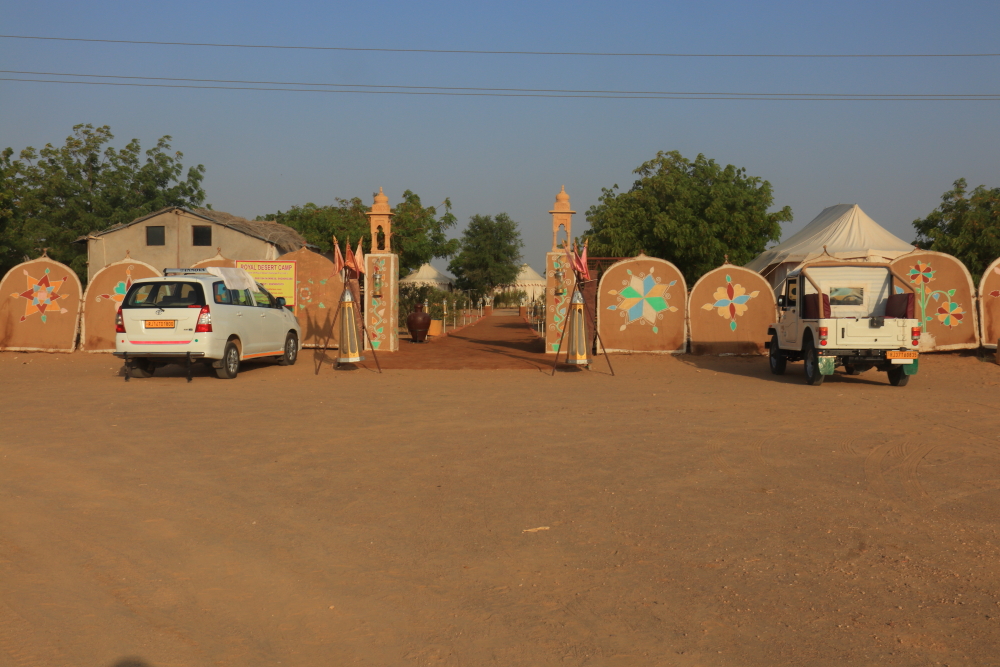 An image showing exterior of Royal Desert Camp in Sam. A tourist cab and a jeep are standing beside the entry gate. The entry gate is nicely decorated in accordance with the ambience of the desert camp.