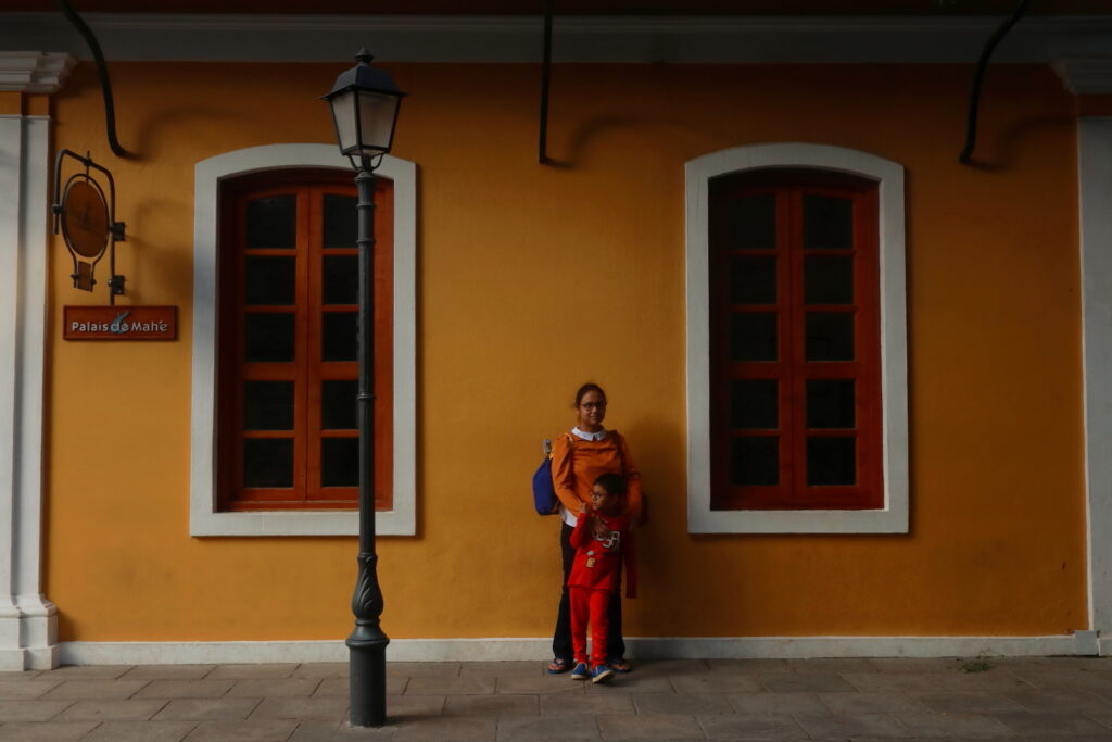 The vibrant yellow wall of Palais De Mahe hotel acts as perfect background for a portrait.
