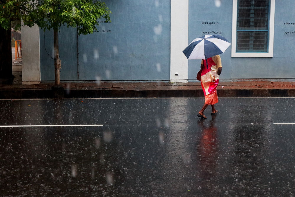 A lady walking in the rain on a Pondicherry Street with an umbrella in hand